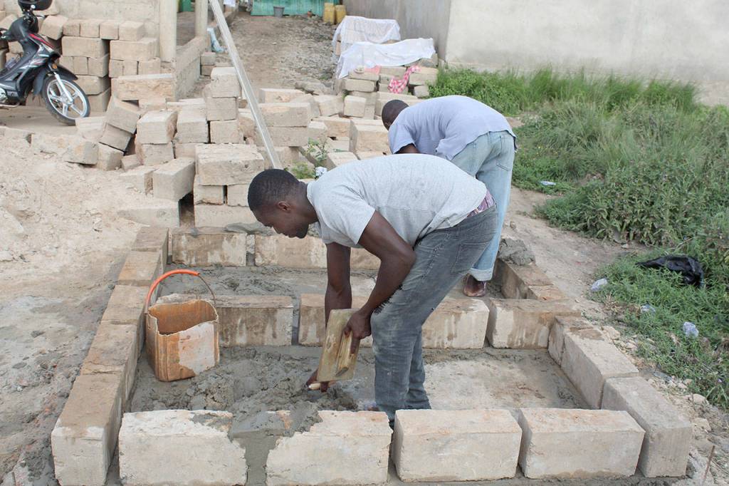 Two unidentified bricklayer apprentices work on a toilet.