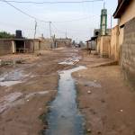 The main residential road in Zogbedgi is packed dirt. Drains from outdoor shower stalls keep the roadway wet even in the dry season.