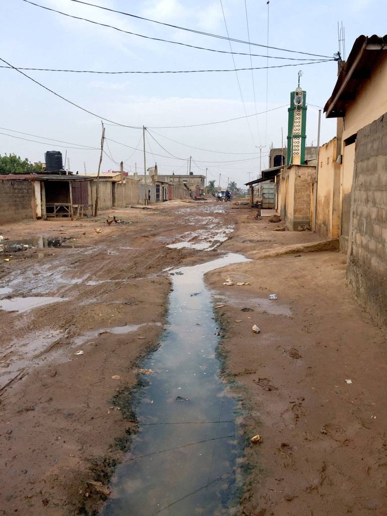 The main residential road in Zogbedgi is packed dirt. Drains from outdoor shower stalls keep the roadway wet even in the dry season.