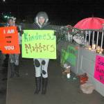 Maariyah Dugan, right, and Siouxzie Hinton stand in the rain last week on the Valley Creek bridge in Port Angeles to protest the lack of suicide barriers on the span and to urge people to be more compassionate to one another. (Paul Gottlieb/Peninsula Daily News)