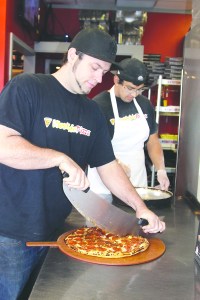 Westside Pizza owner Tanner Stephens slices a pizza at his restaurant's new location at 612 S. Lincoln St. in Port Angeles. Benny Vincent is in the background greasing pans.