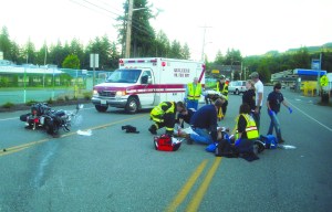 Christoper Loper of Yelm is attended to by emergency personnel Saturday night in Quilcene as his Harley-Davidson motorcycle lies in the middle of U.S. Highway 101. Margaret McKenzie/Peninsula Daily News