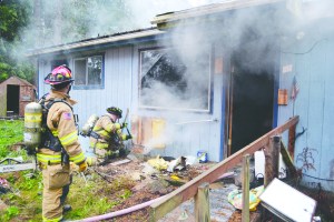 Firefighters with east Jefferson County Fire-Rescue use a chain saw and Halligan tool to cut away the siding on the structure on Gene Street in Port Townsend to reach flames that had extended below the floor.  Bill Beezley/East Jefferson County Fire-Rescue