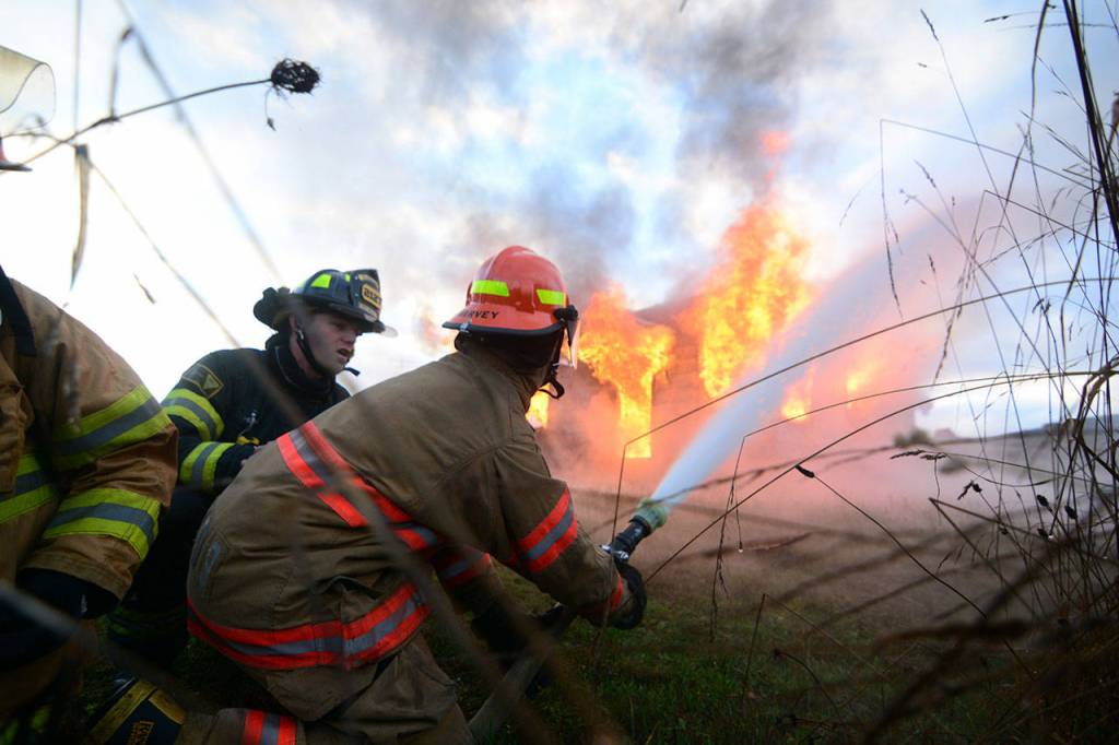 Firefighter Tyler Gear of Clallam County Fire District No. 2 coaches 16-year-old Brandon Harvey as he sprays water during the live fire training. (Jesse Major/Peninsula Daily News)