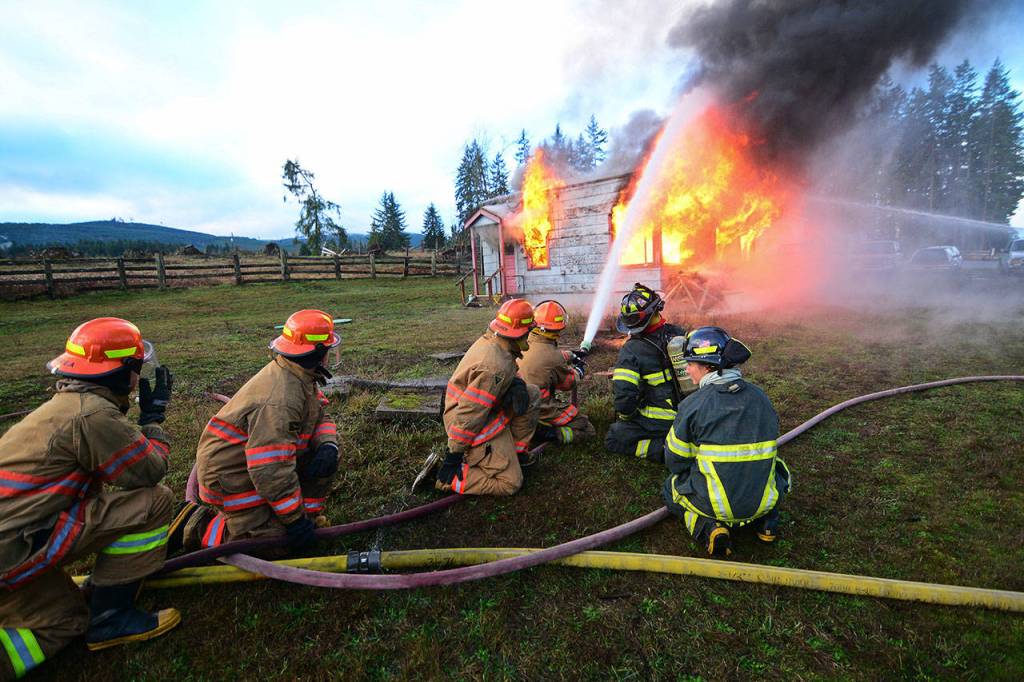 Firefighters coach youths in the Fire Explorer Scouts program as they put water on a burning building during the training. (Jesse Major/Peninsula Daily News)
