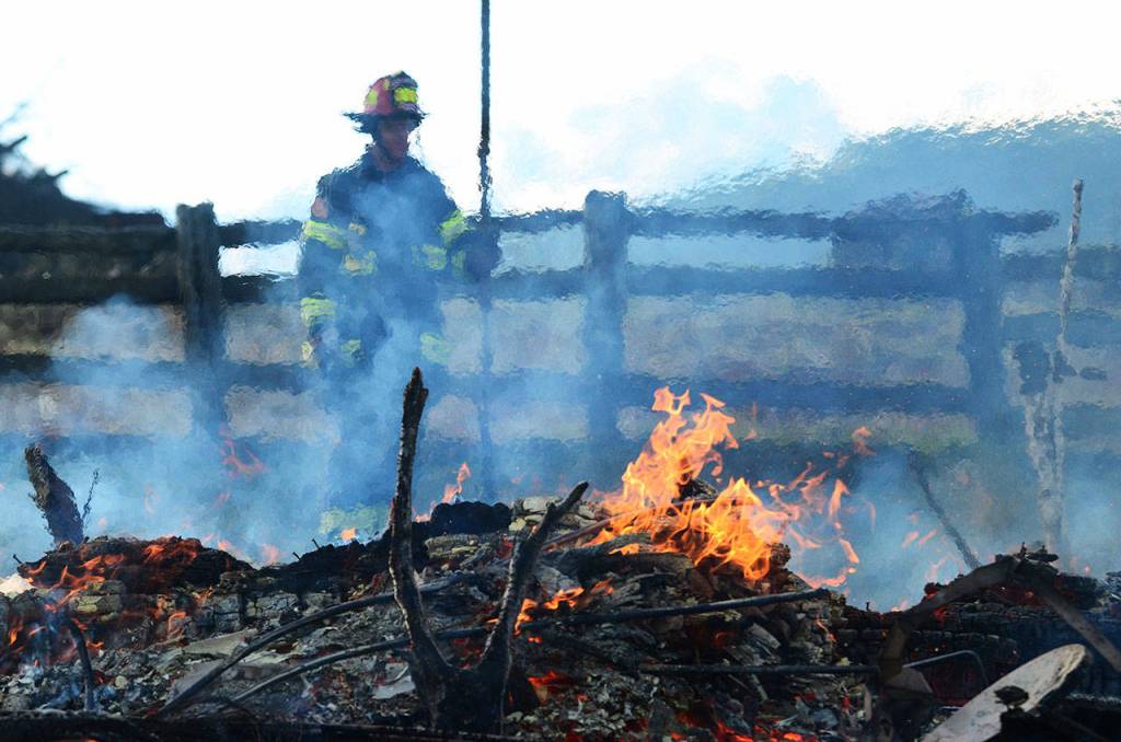 A firefighter watches over the burning remains of a house that firefighters burned during a training day Sunday. (Jesse Major/Peninsula Daily News)