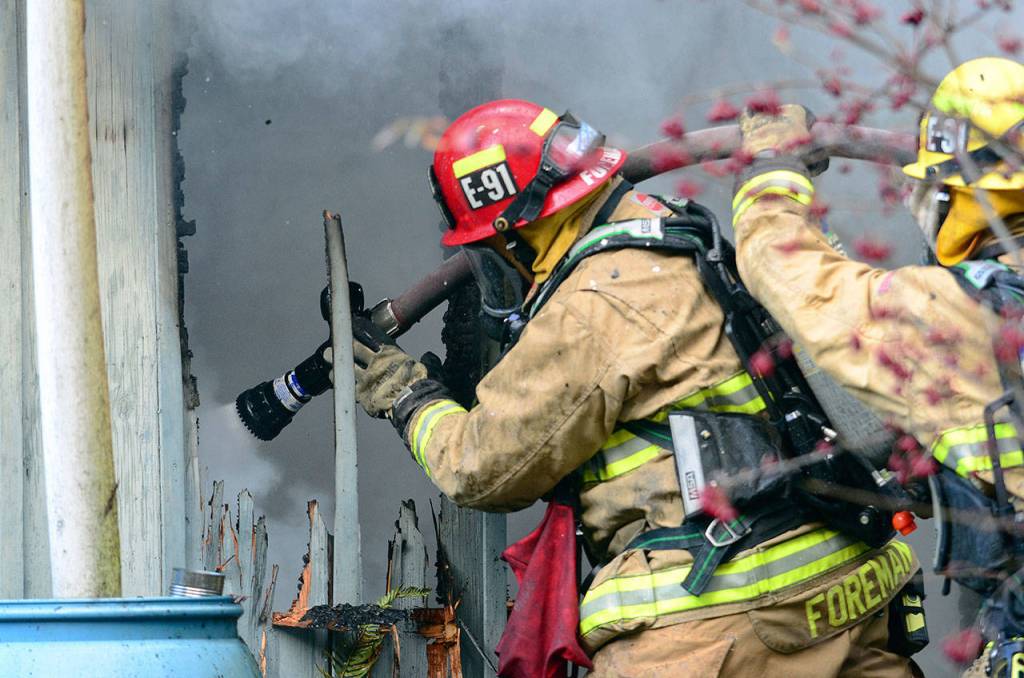 A firefighter sprays down the home Thursday morning. (Jesse Major/Peninsula Daily News)