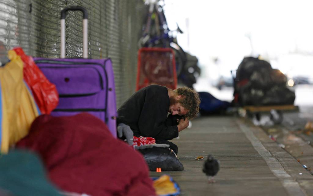 Dominic, who battles mental illness, sits on a sidewalk under the Smith Ave. Bridge in Everett on Oct. 12. The area is a constant gathering place for homeless people battling addiction and mental illness. Dominic has been identified as one of the top chronic and costliest users of emergency and other services in Everett, but despite the efforts of a specialized team of experts, he remains on the streets. (Ted S. Warren/The Associated Press)
