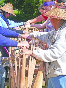 With workers gathered around a baidarka with their hands on the keel