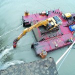 A tethered barge carrying an excavator with a jackhammer attachment chips away at the precipice as water flows over the Glines Canyon Dam.  -- Photo by Keith Thorpe/Peninsula Daily News