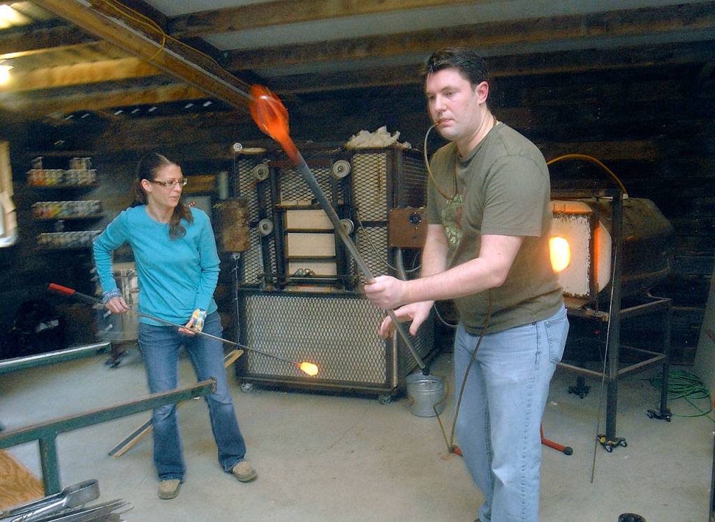 Megan Schmidlkofer, left, and her mentor, Wes Fetch, work together to create a collaborative blown-glass decoration at Schmidlkofers Molten Mommas Hot Shop in rural Sequim. (Keith Thorpe/Peninsula Daily News)