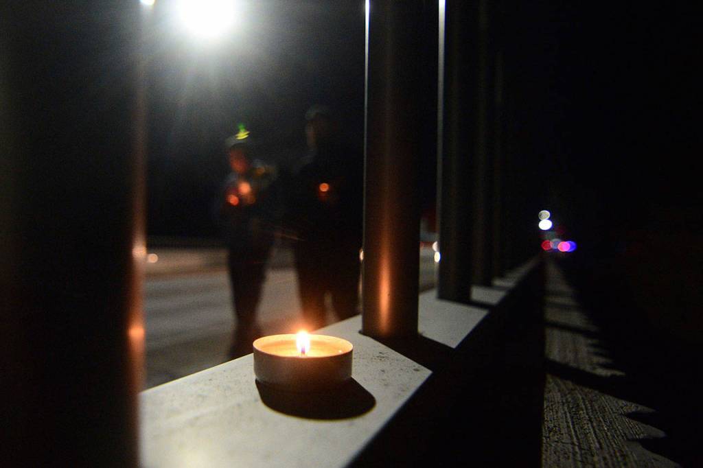 People walk past a flickering candle along the Valley Creek Eighth Street Bridge in Port Angeles Wednesday during a vigil mourning community members who have committed suicide. (Jesse Major/Peninsula Daily News)
