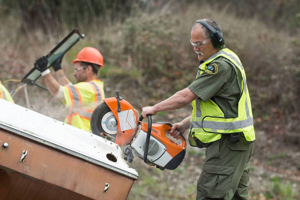 Deputy Nate Pence cuts through an abandoned boat near Sequim on Wednesday. Inmates on the Clallam County Chain Gang are not allowed to use powered saws. (Jesse Major/Peninsula Daily News)