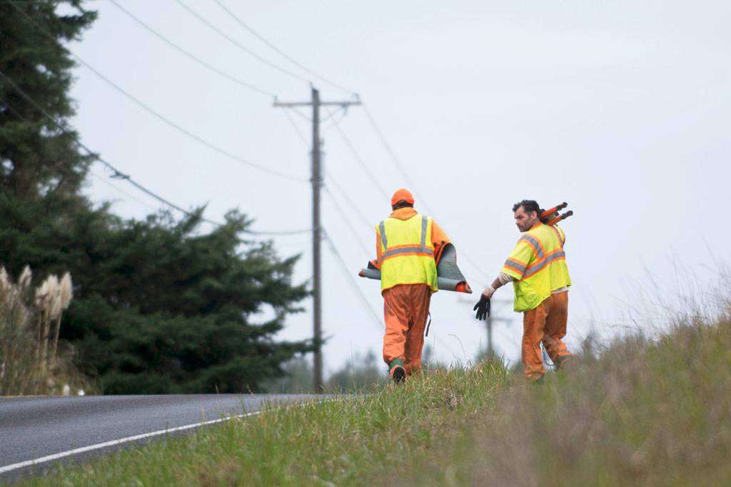 Clallam County jail inmates set up signs along Towne Road near Sequim before tearing apart an abandoned boat on Wednesday. (Jesse Major/Peninsula Daily News)