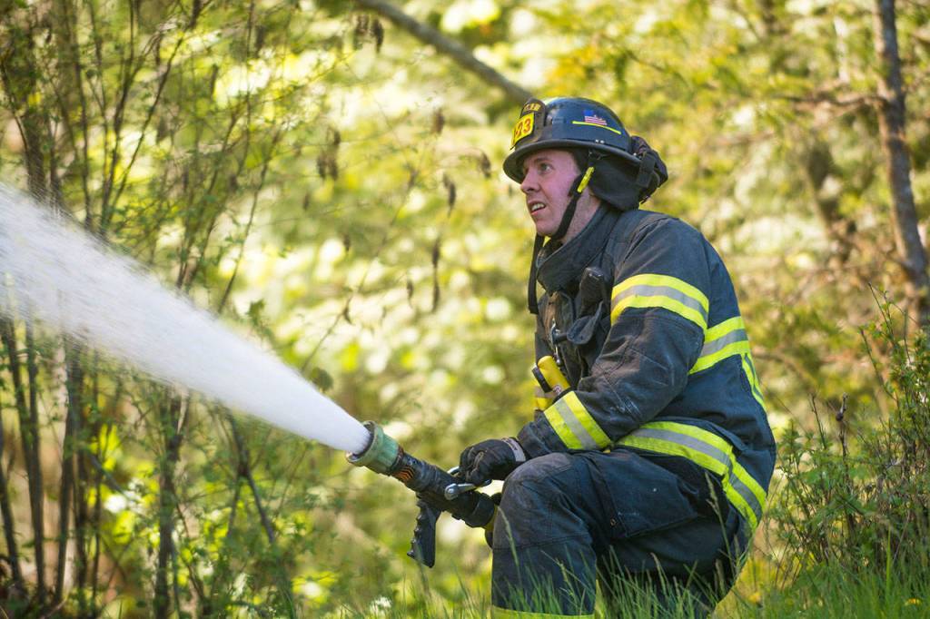 Firefighter Sean Charon puts water on the burning house. (Jesse Major/Peninsula Daily News)