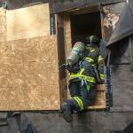 A firefighter with Clallam County Fire District No. 2 climbs through a firefighter-made window during the training. (Jesse Major/Peninsula Daily News)