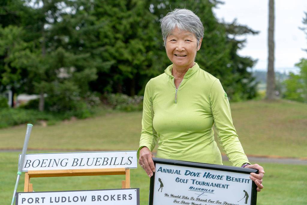 Barbara Berthiaume, co-chair of Dove House Benefit Golf Tournament, places sponsor signs on the tee box on one of the holes used in the tournament. (Steve Mullensky/for Peninsula Daily News)