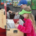 Siblings Finley Rapelje, 8, front, and Mason Rapelje, 9, both of Port Angeles, leaf through a collection of artworks at a vendor booth set up by Fun Whimsical Art of Puyallup on Saturday at the Juan de Fuca Festival of the Arts. (Keith Thorpe/Peninsula Daily News)