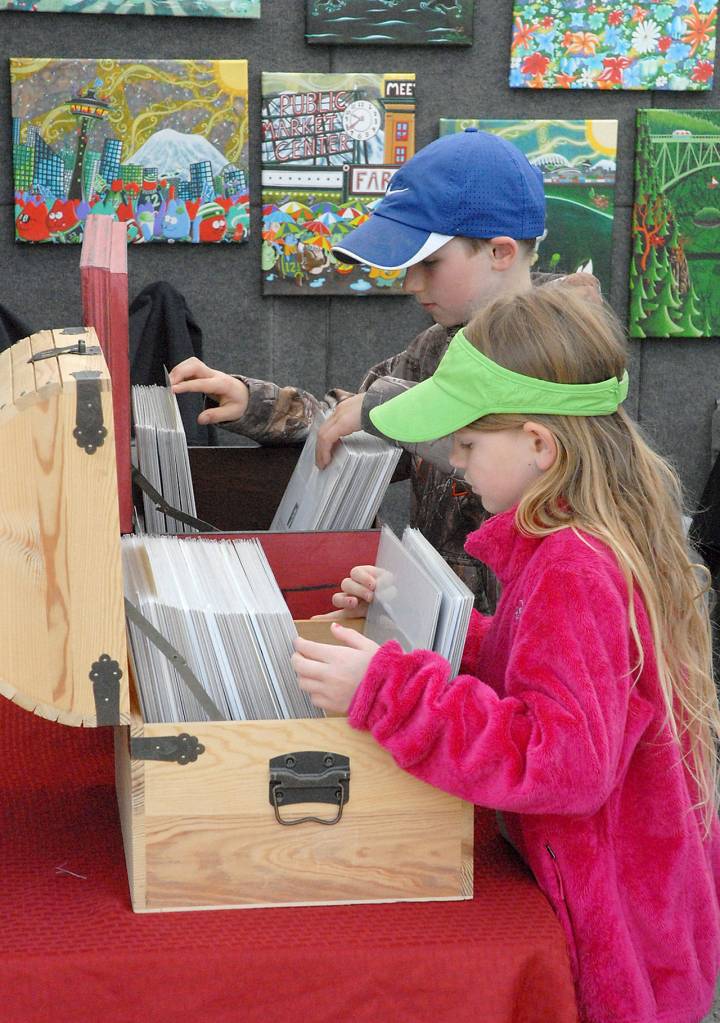 Siblings Finley Rapelje, 8, front, and Mason Rapelje, 9, both of Port Angeles, leaf through a collection of artworks at a vendor booth set up by Fun Whimsical Art of Puyallup on Saturday at the Juan de Fuca Festival of the Arts. (Keith Thorpe/Peninsula Daily News)
