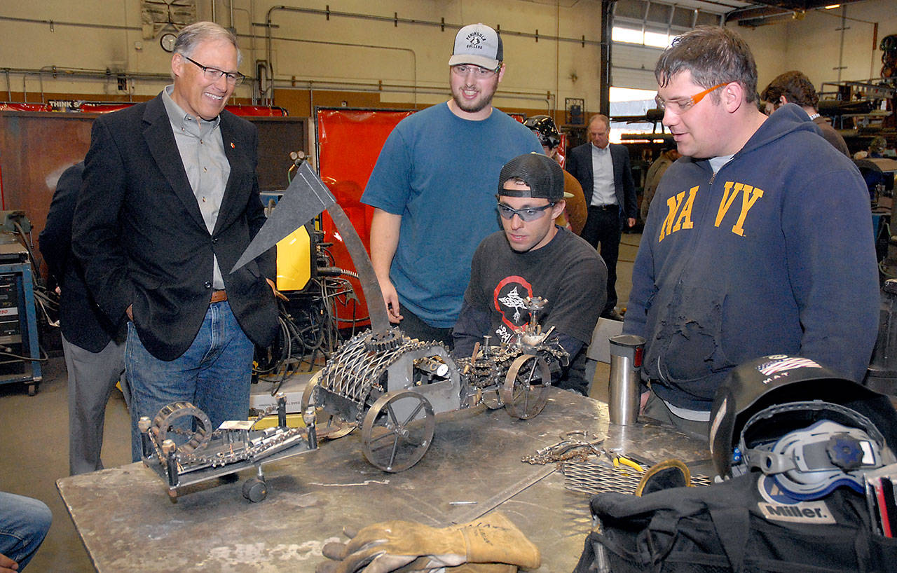 Washington Gov. Jay Inslee, left, examines a steampunk-themed metal artwork created by Peninsula College welding students, from left, Ellis Henderson of Port Townsend, and Nathan Hofer and Matthew Weaver of Port Angeles during the governors tour of the colleges welding class on the Port Angeles campus on Thursday. The shop tour was part of a presentation on economic opportunities and partnerships in the maritime industries on the North Olympic Peninsula. (Keith Thorpe/Peninsula Daily News)