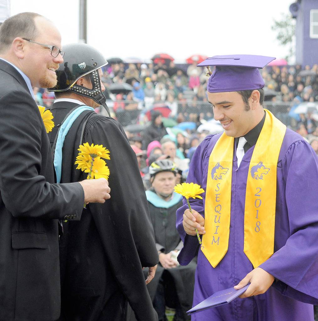 Sequim High School graduate Nick Janikic receives his diploma from Principal Shawn Langston (in helmet) and a flower from Sequim School Board Director Brian Kuh. High school staff donned helmets at Friday nights graduation in support of teacher Jon Eekhof, who is recovering from head injuries sustained in a fall earlier this year. (Michael Dashiell/Olympic Peninsula News Group)