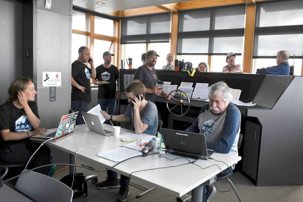 The R2AK War Room at the Northwest Maritime Center hums with activity in the early hours of Stage One. Race Boss Daniel Evans, standing second from right, said his team is constantly monitoring the racers vessels, position, and well-being. Over 45 volunteers play roles in the safety of the participants. (Jeannie McMacken/Peninsula Daily News)