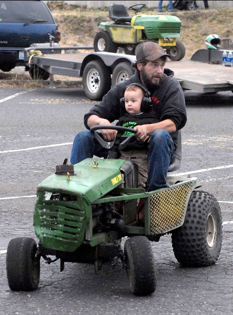 Adam Coile of Port Townsend rides a souped-up lawn mower with his son, Christopher Cole, 1 1/2, during warm-ups for Wednesdays mower races in Port Angeles. (Keith Thorpe/Peninsula Daily News)
