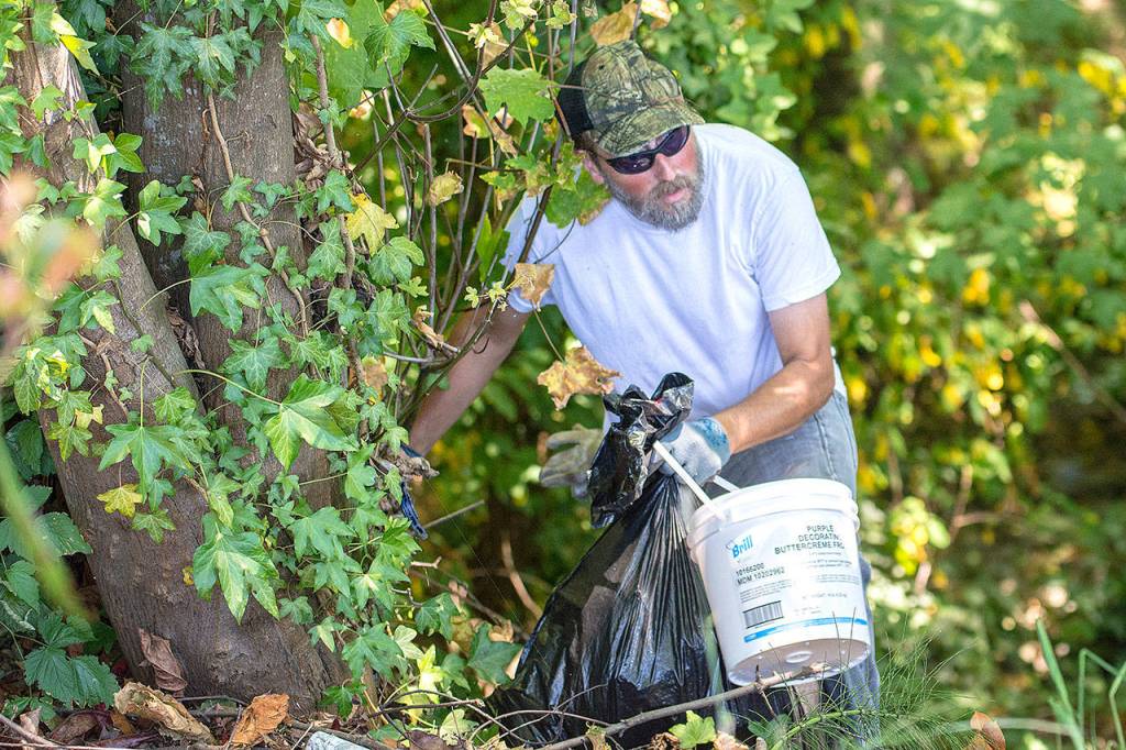 Roger Bogers carries trash out of a ravine near Lincoln Street in Port Angeles on Sunday. (Jesse Major/Peninsula Daily News)
