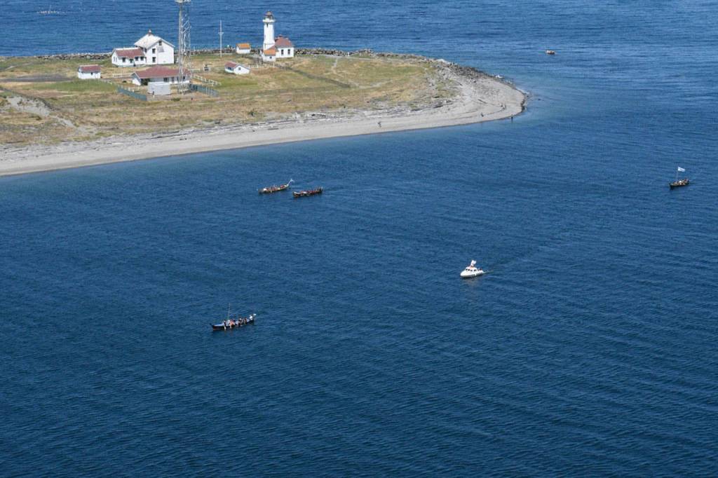 Canoes pass the Point Wilson Lighthouse on their way to a landing at the Fort Worden beach on Monday. (Jeannie McMacken/Peninsula Daily News)