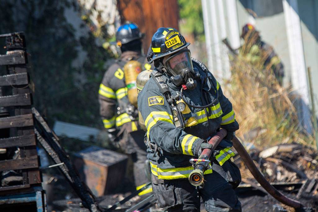 A firefighter caries a hose as firefighters battle an RV fire on the 2300 block of East Fifth Avenue in Port Angeles on Sunday. (Jesse Major/Peninsula Daily News)