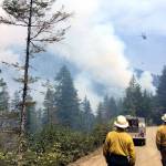 Firefighters approach the Maple Fire in Mason County as a helicopter in the distant sky drops water on it. (State Department of Natural Resources)
