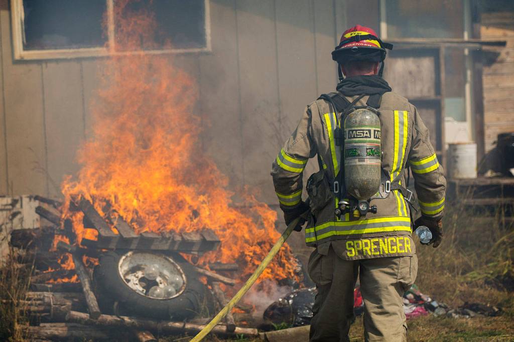 Lt. Mike Springer carries a hose toward burning debris outside a house and trailer fire at the corner of Blue Mountain Road and School House Lane on Tuesday afternoon. (Jesse Major/Peninsula Daily News)