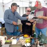 Jeff Boster of Port Angeles describes the features of a meat slicer to Zoay Rees and Josh Rees of Sequim oat Bosters display of goods near the Joyce Museum in Joyce during the 2017 Great Strait Sale. (Keith Thorpe/Peninsula Daily News)