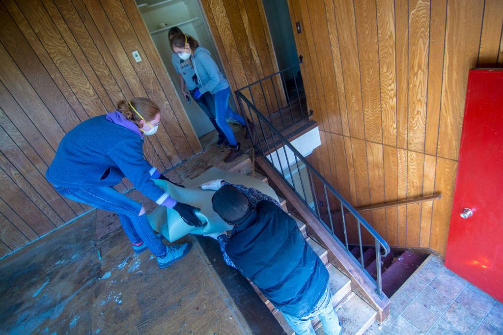 Volunteers remove carpet from a stairwell at a soon-to-be Oxford House on Saturday. (Jesse Major/Peninsula Daily News)