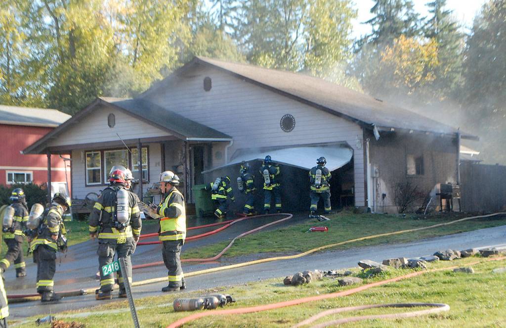 Clallam County Fire District No. 2 firefighters remove the garage door to gain access to a house at 2414 W. Edgewood Drive near Port Angeles on Tuesday after intense heat from a fire next door ignited the siding and flames spread into the attic. (Keith Thorpe/Peninsula Daily News)