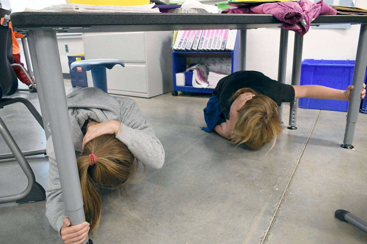 Kaida Rodrigues, left, and Kaleb Kruse tucked under their desks Thursday at Salish Coast Elementary School for the Great Washington ShakeOut. (Jeannie McMacken/Peninsula Daily News)