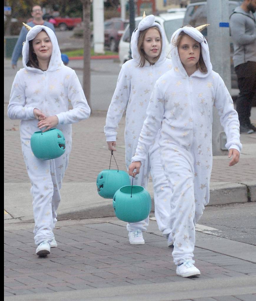 Dressed as a trio of unicorns, Brooklyn Johnson, Cayleigh Alward and Teanna Clark, all 10 from Port Angeles, march across Front Street in search of Halloween candy. (Keith Thorpe/Peninsula Daily News)