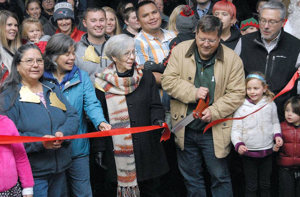 Marc Abshire, executive director of the Port Angeles Regional Chamber of Commerce, center left, cuts the ribbon to officially open the skating rink at the Port Angeles Winter Ice Village on Friday evening. Among those holding the ribbon were, from left, Lower Elwha Klallam Tribe Chairwoman Frances Charles, Port Angeles Mayor Sissi Bruch, and Necessities and Temptations business owner Edna Peterson. (Keith Thorpe/Peninsula Daily News)