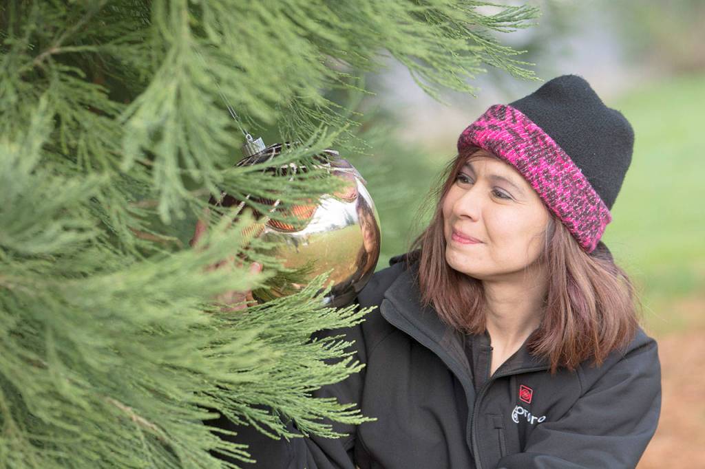 Lydia Kores of Port Angeles shows one of the ornaments that protestors have hung on the sequoia tree at Lions Park in Port Angeles on Monday. (Jesse Major/Peninsula Daily News)