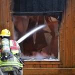 Firefighter/EMT Kjel Skov sprays the inside of a deck spanning from a house fire that erupted on Monday morning in Blyn. (Matthew Nash/Olympic Peninsula News Group)
