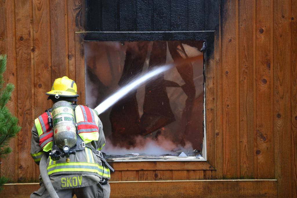 Firefighter/EMT Kjel Skov sprays the inside of a deck spanning from a house fire that erupted on Monday morning in Blyn. (Matthew Nash/Olympic Peninsula News Group)
