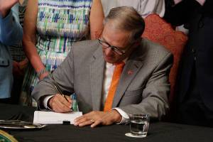 In this July 5, 2017 file photo, Washington Gov. Jay Inslee signs into law a measure that makes Washington one of a hand full of states that guarantee paid family leave in Olympia, Wash. Employers and employees in Washington state will start paying into a new paid family leave program next week, and benefits from the program will begin in 2020. (AP Photo/Rachel La Corte, file)