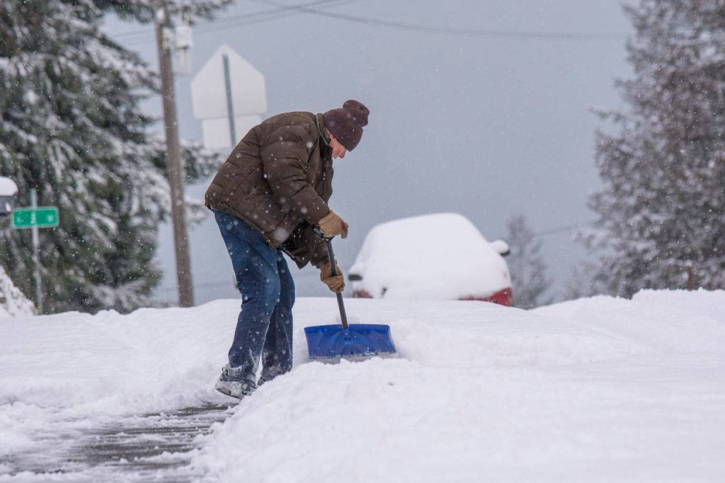 Richard Miller shovels snow from the sidewalk on Eighth Street in Port Angeles as snow continued to fall Monday morning. He said he planned to help a couple neighbors clear snow from their driveways as well. (Jesse Major/Peninsula Daily News)