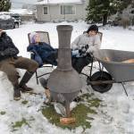 Not detoured by a landscape covered with a blanket of snow, Dan Callahan, Brenna Callahan, 10, and Emily Callahan bask in the heat of a portable wood stove set up next to the street near their home at Fifth and Oak streets in Port Angeles on Saturday. Dan Callahan said it was an ideal way to spend an afternoon people watching and enjoying the cold winter air. (Keith Thorpe/Peninsula Daily News)