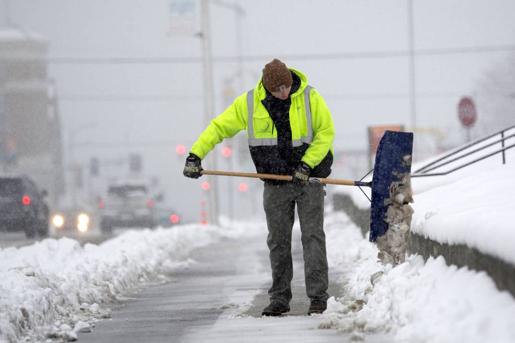 Clallam County maintenance worker Ryan Heskett clears the sidewalk in front of the Clallam County Courthouse as snow begins to fall Monday. (Jesse Major/Peninsula Daily News)