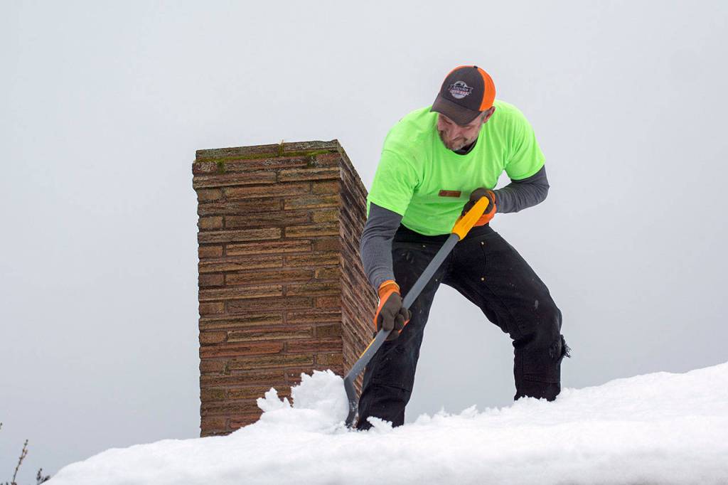 Greg Olekas, who organized a work party to clear snow from a long time Port Angeles coachs home, clears snow from his roof Tuesday. About 20 people showed up to help. (Jesse Major/Peninsula Daily News)