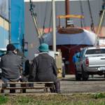 Two people sitting on pallets watch as the schooner Adventuress is lifted Friday. (Jesse Major/Peninsula Daily News)