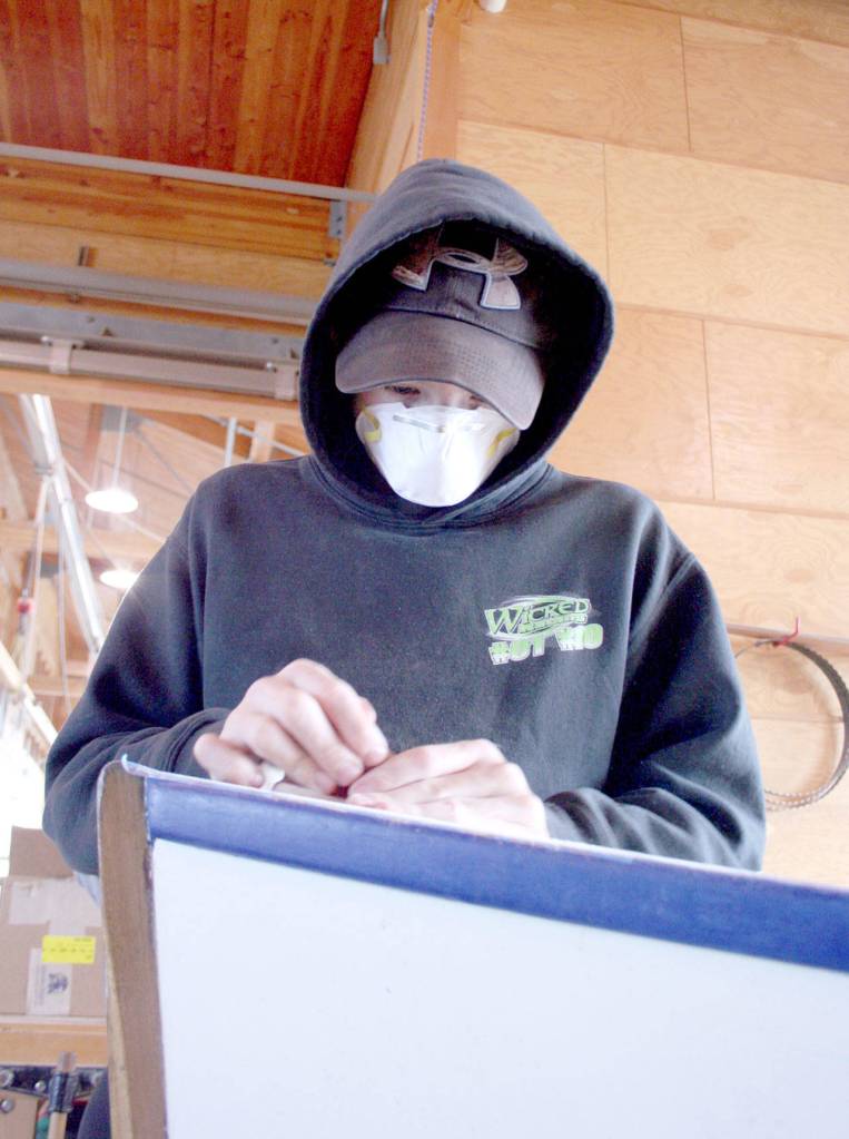 Caeleb Warwick works on the front of a wooden boat, manually sanding away the varnish Wednesday at the Northwest Maritime Center. (Brian McLean/Peninsula Daily News)