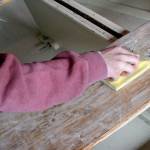 Briana Martin pushes sandpaper with the grain to strip away the varnish on a wooden boat Wednesday at the Northwest Maritime Center. (Brian McLean/Peninsula Daily News)