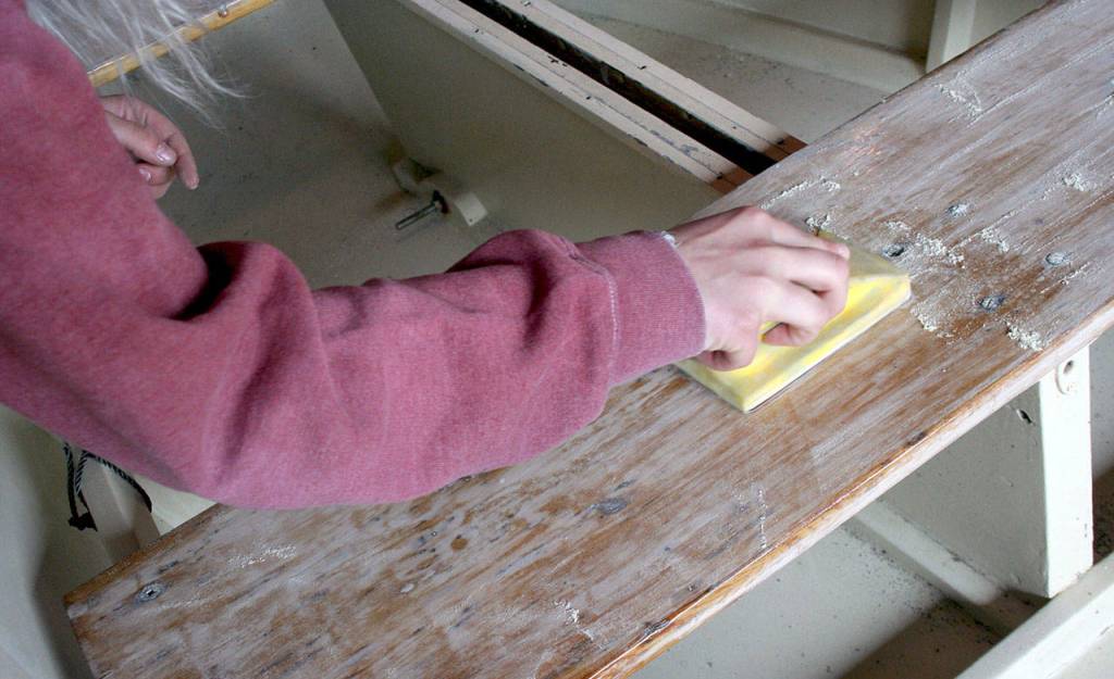 Briana Martin pushes sandpaper with the grain to strip away the varnish on a wooden boat Wednesday at the Northwest Maritime Center. (Brian McLean/Peninsula Daily News)
